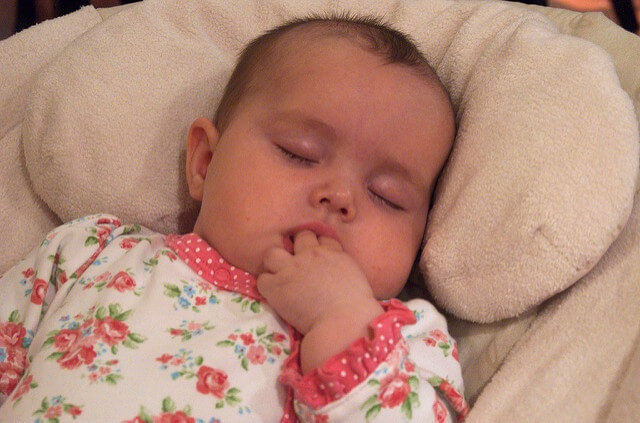 A sleeping baby chews her fingers