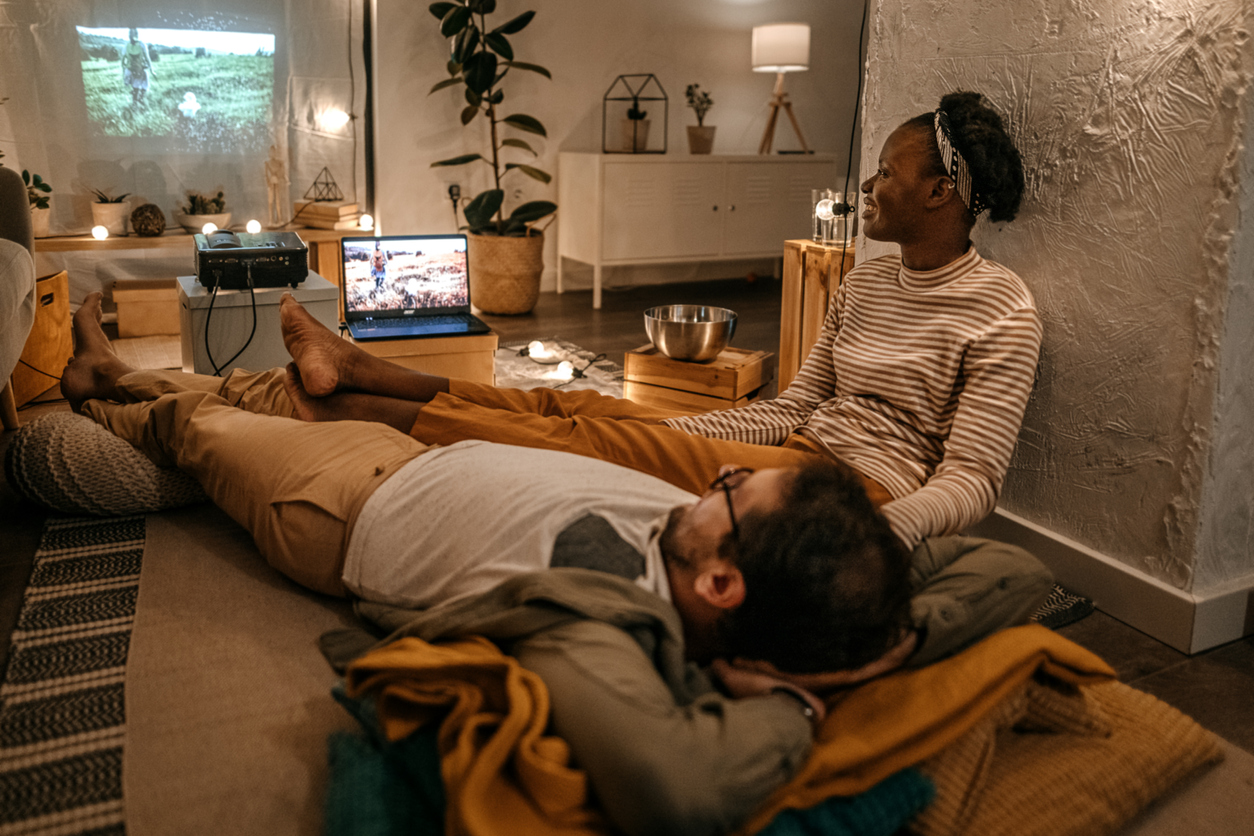 Romantic young couple lying and sitting on flooring watching a movie on their large projector screen at home