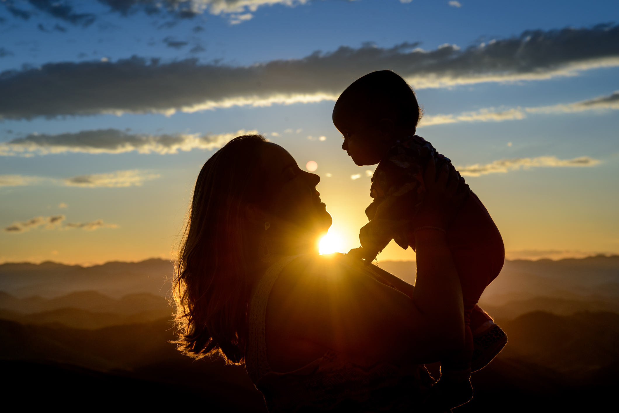 baby held up to the sky by mom at sunset 
