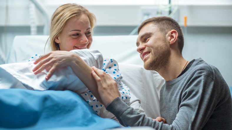 In the Hospital Mother Holds Newborn Baby, Supportive Father Lovingly Hugs Baby and Wife. Happy Family in the Modern Delivery Ward.