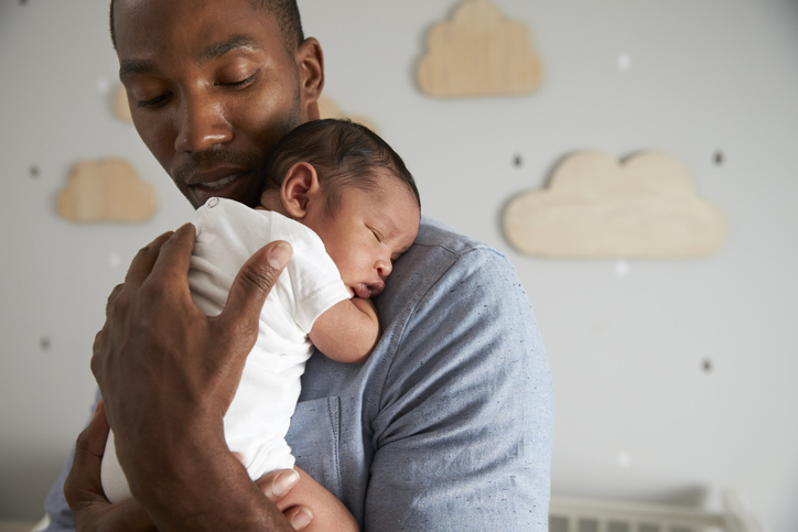 Dad holds infant baby in nursery; skin-to-skin contact between baby and dad.