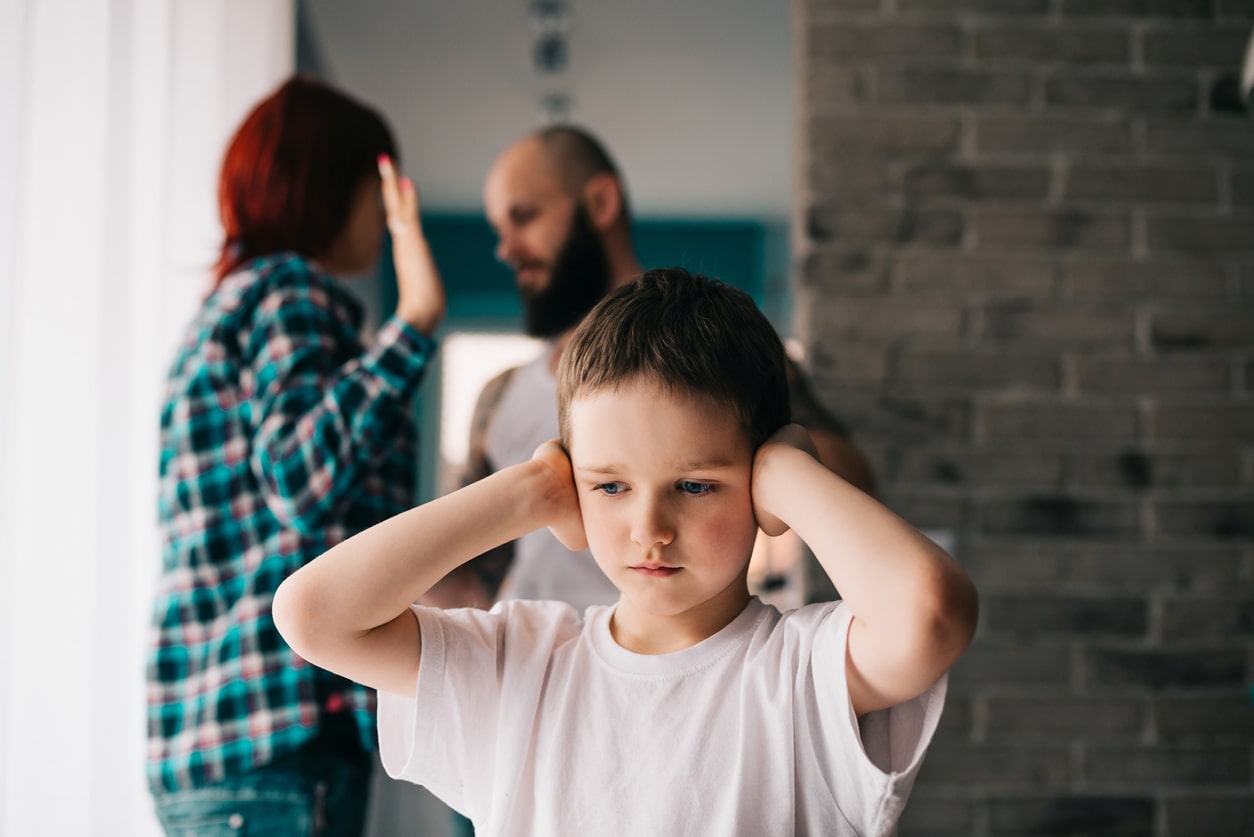 Sad child covering his ears with hands during divorced parents quarrel.