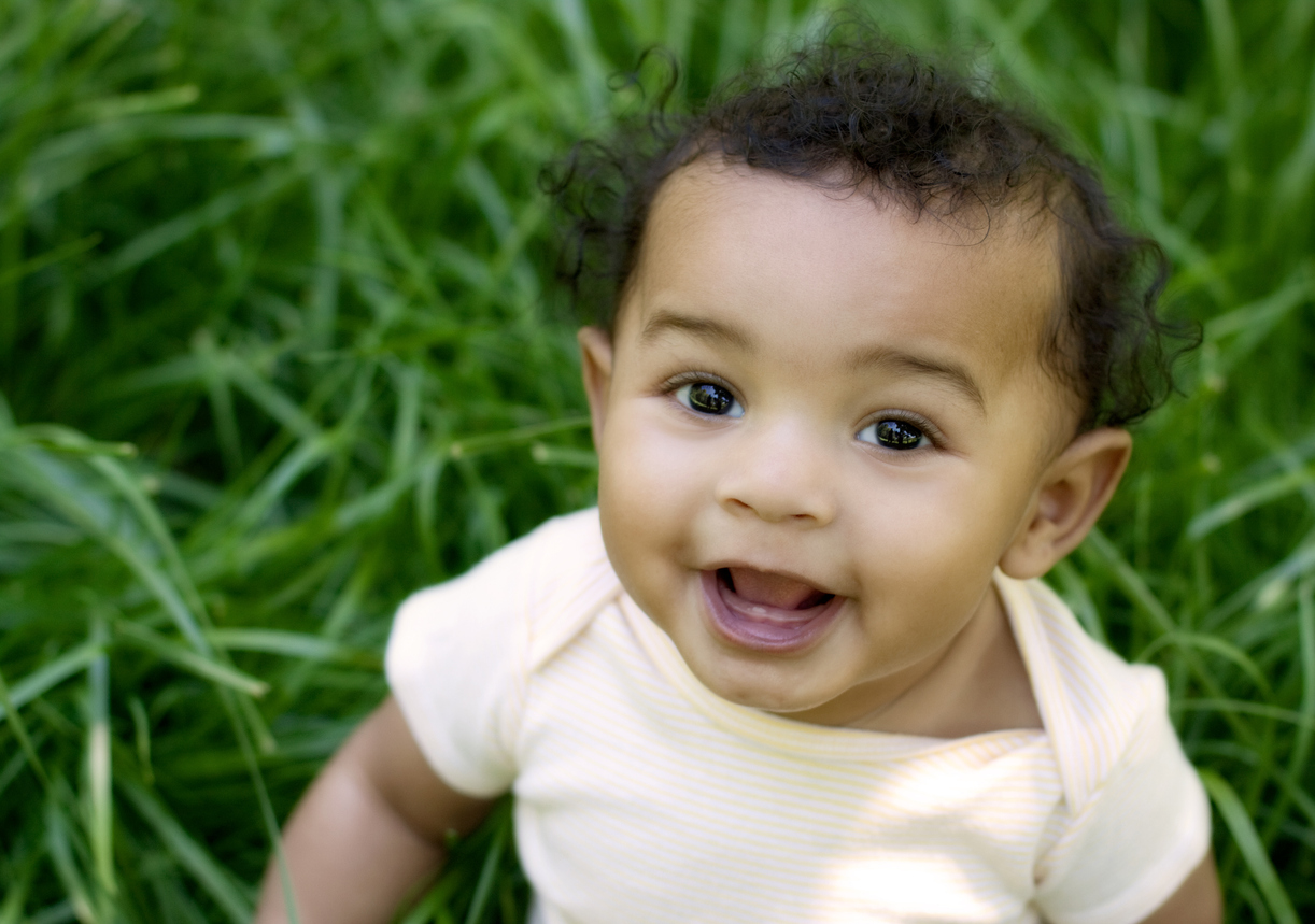 Adorable baby looking up from grass. Mixed race.