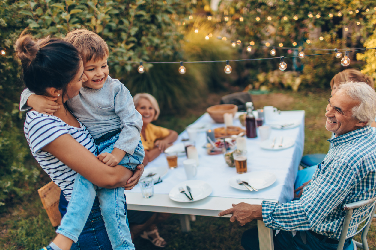 hoto of a multi-generation family having dinner outdoors in their back yard