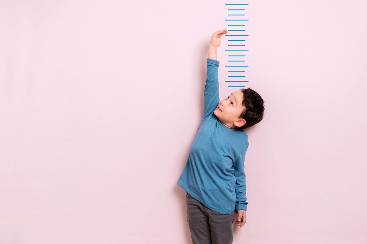 Little boy measures his height against a pink wall.