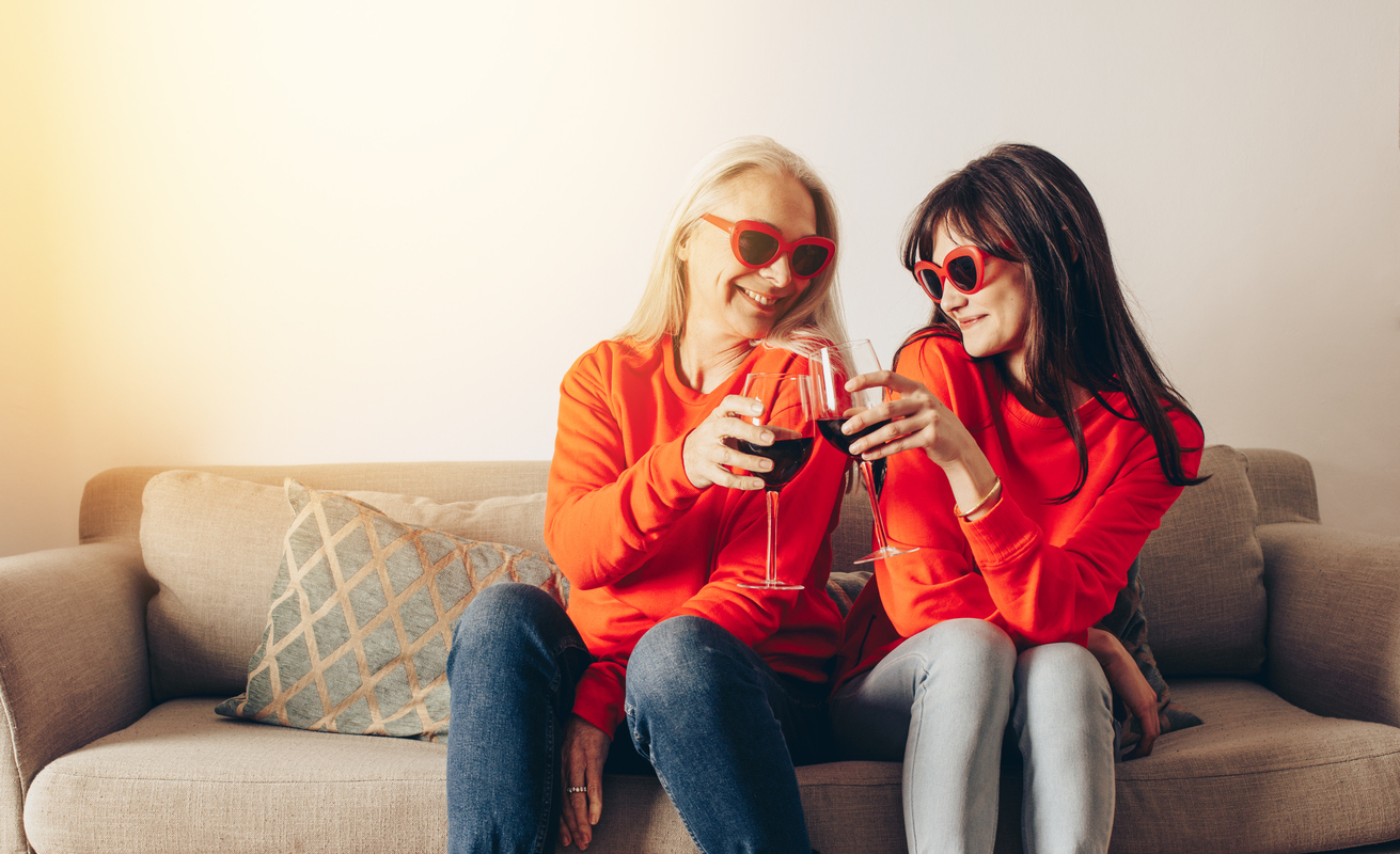Two women wearing similar outfit toasting glasses of wine sitting at home. 