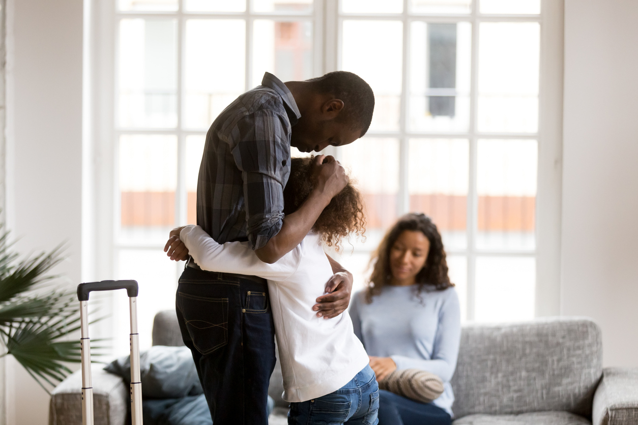 Cute sad little African American girl hug dad standing with suitcase leaving for business trip, upset small mixed race kid embrace father saying goodbye, parents separating. Shared custody concept