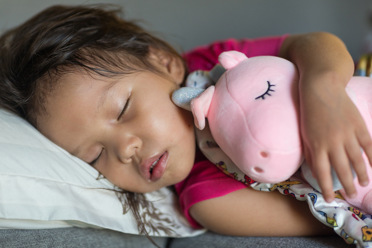 Adorable young female child asleep on a comfortable pillow and bed while cuddling with a pink stuffed animal