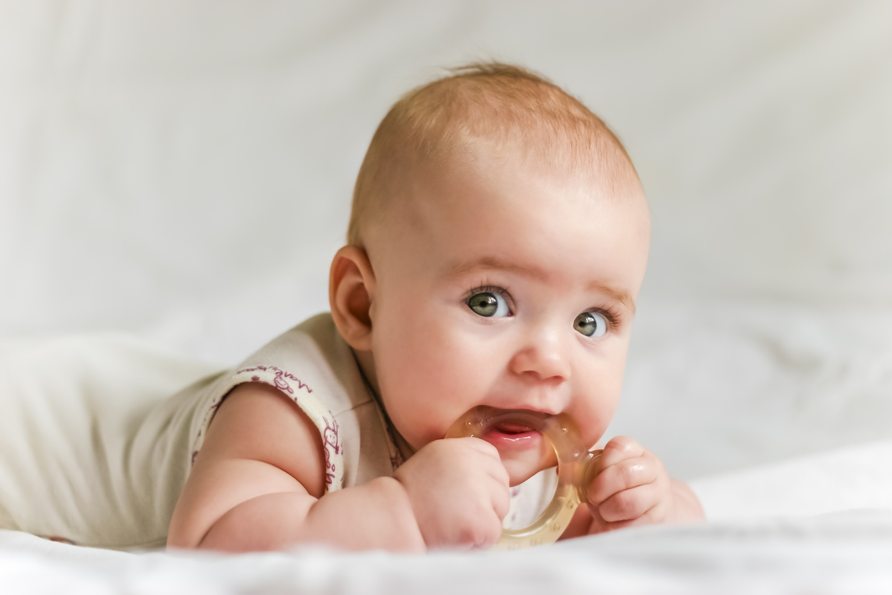 Six-month baby girl on her stomach with teether in the mouth