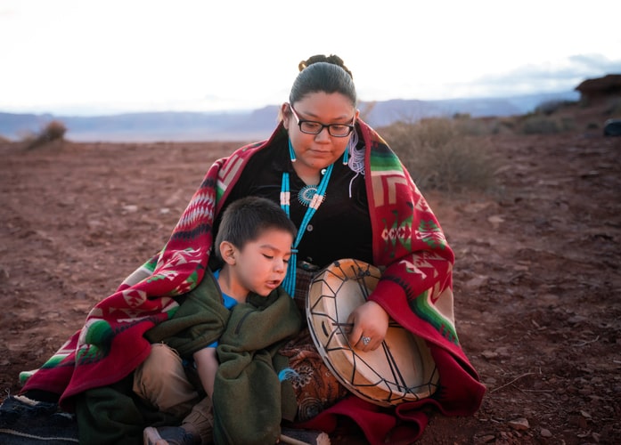 Navajo young woman holding a traditional drum with little brother around campfire on the Arizona desert