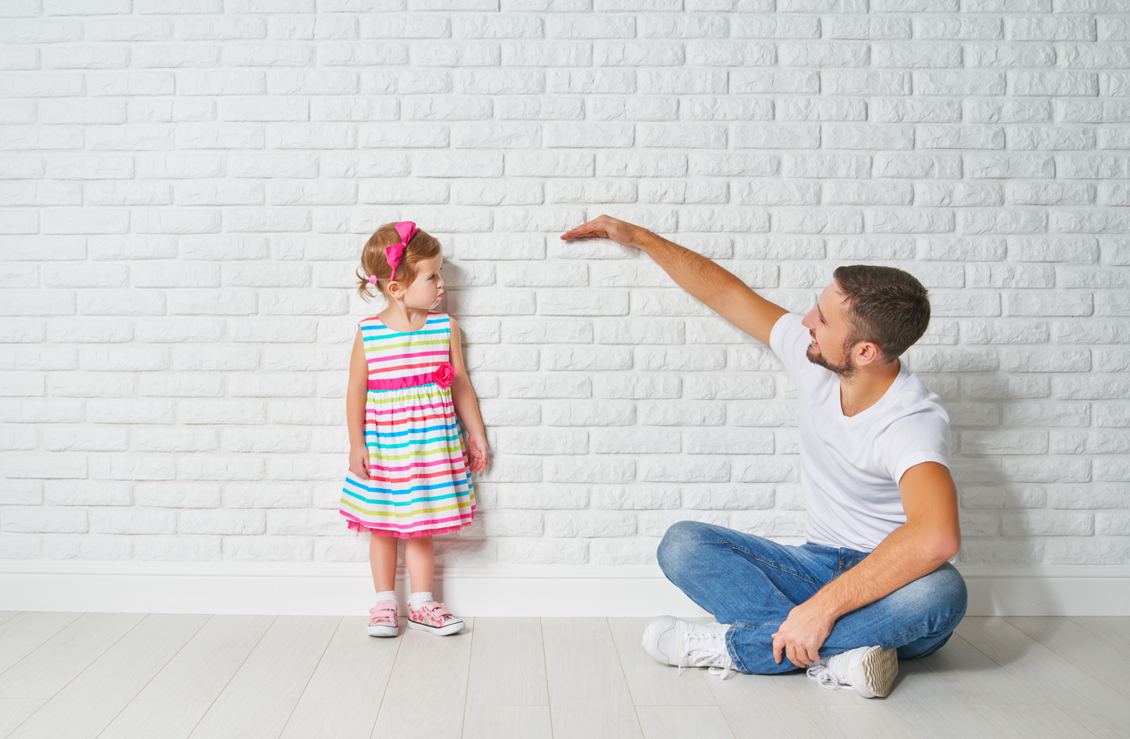Dad measures the growth of her child daughter at a blank brick wall