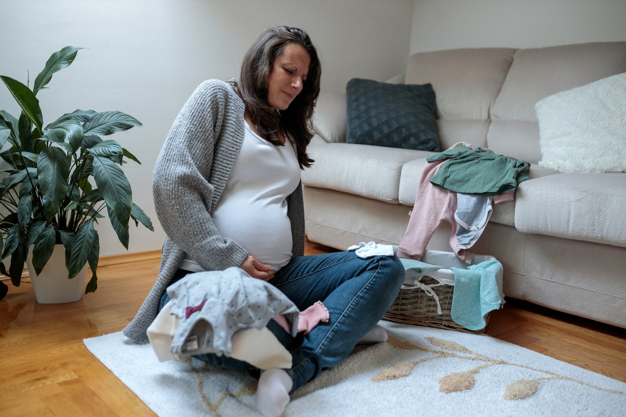 Woman in ninth month of pregnancy experiencing contractions and severe pain sitting in a living room. Time to go to the hospital for labor.