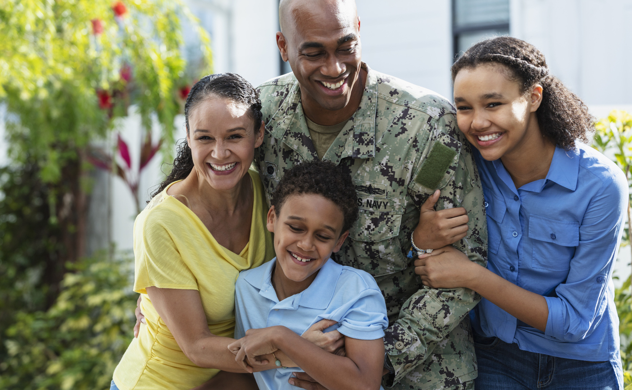 Portrait of a proud African-American navy veteran with his multiracial family, standing together outside their home.