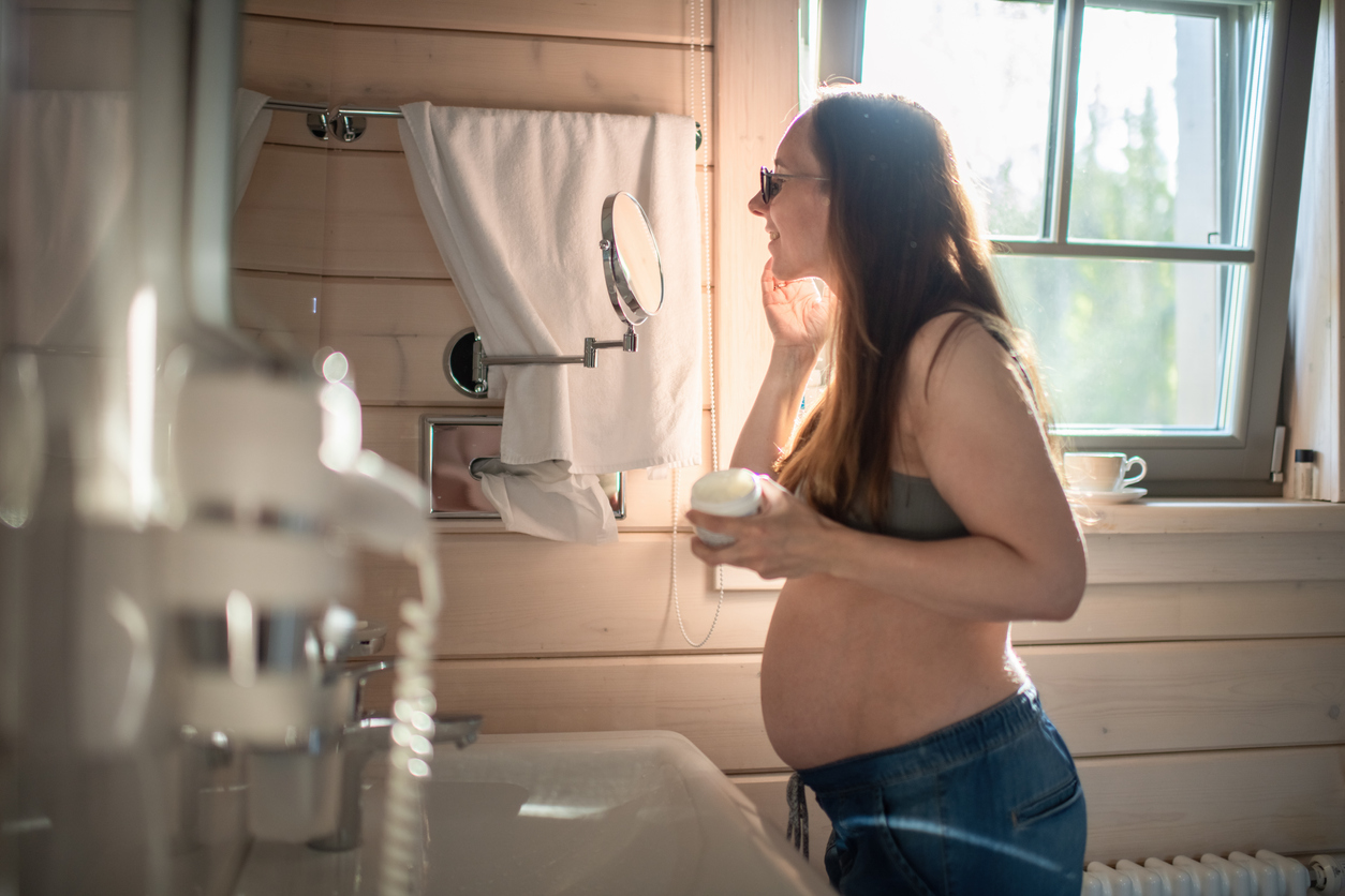 Pregnant woman applying moisturizer in the morning