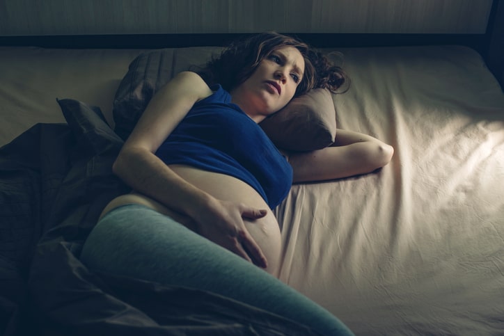 Pregnant woman feeling pain in her belly lying in bed with insomnia at night