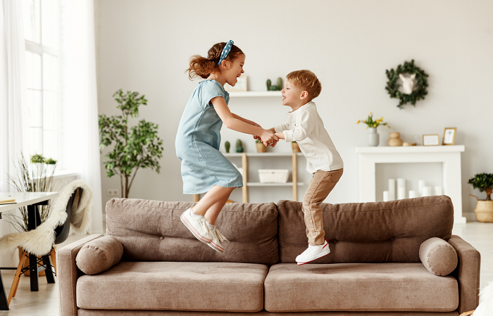 Siblings jumping on sofa in child-safe living room