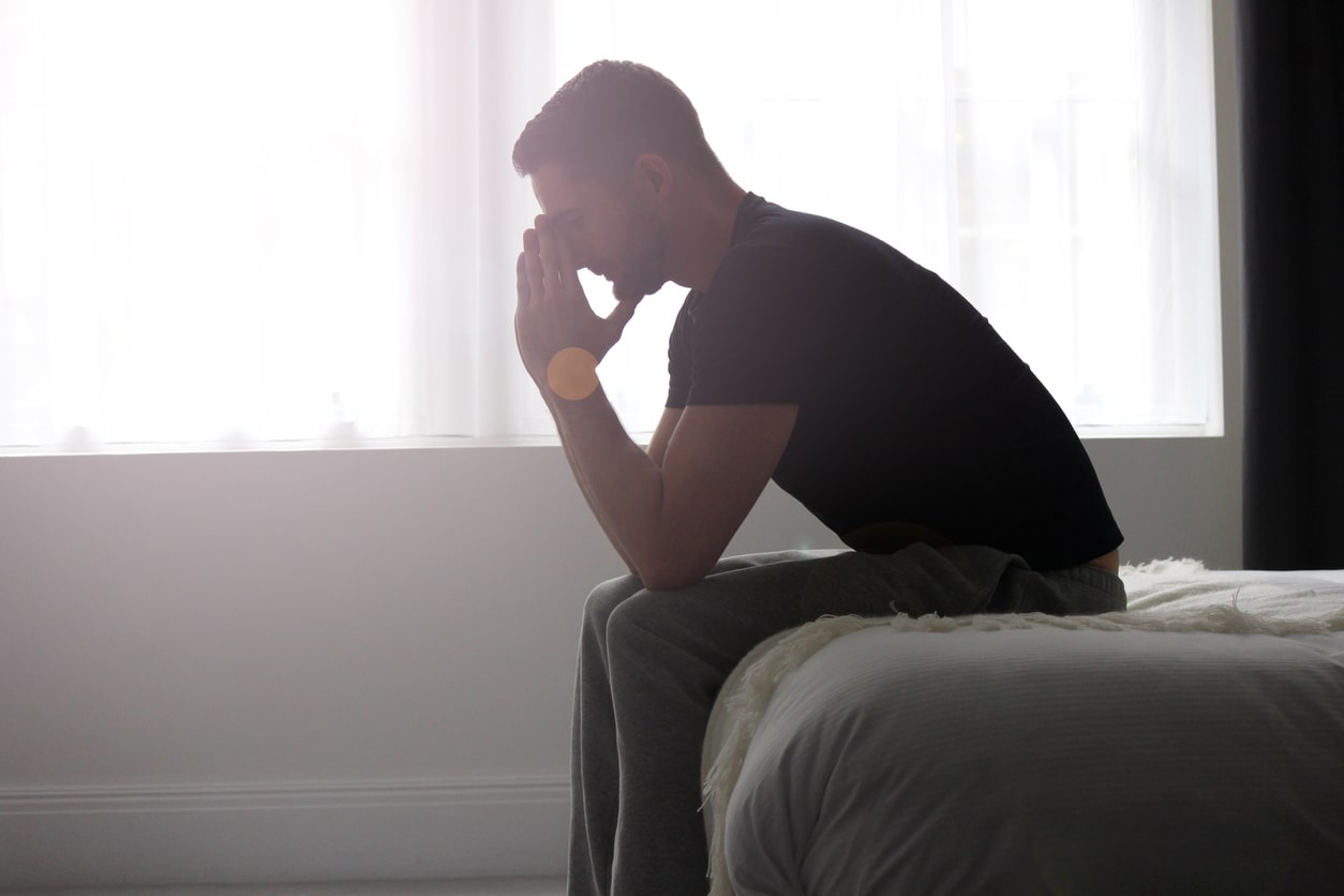 Depressed man sits on his bed with his hands on his head. Victim of domestic abuse.