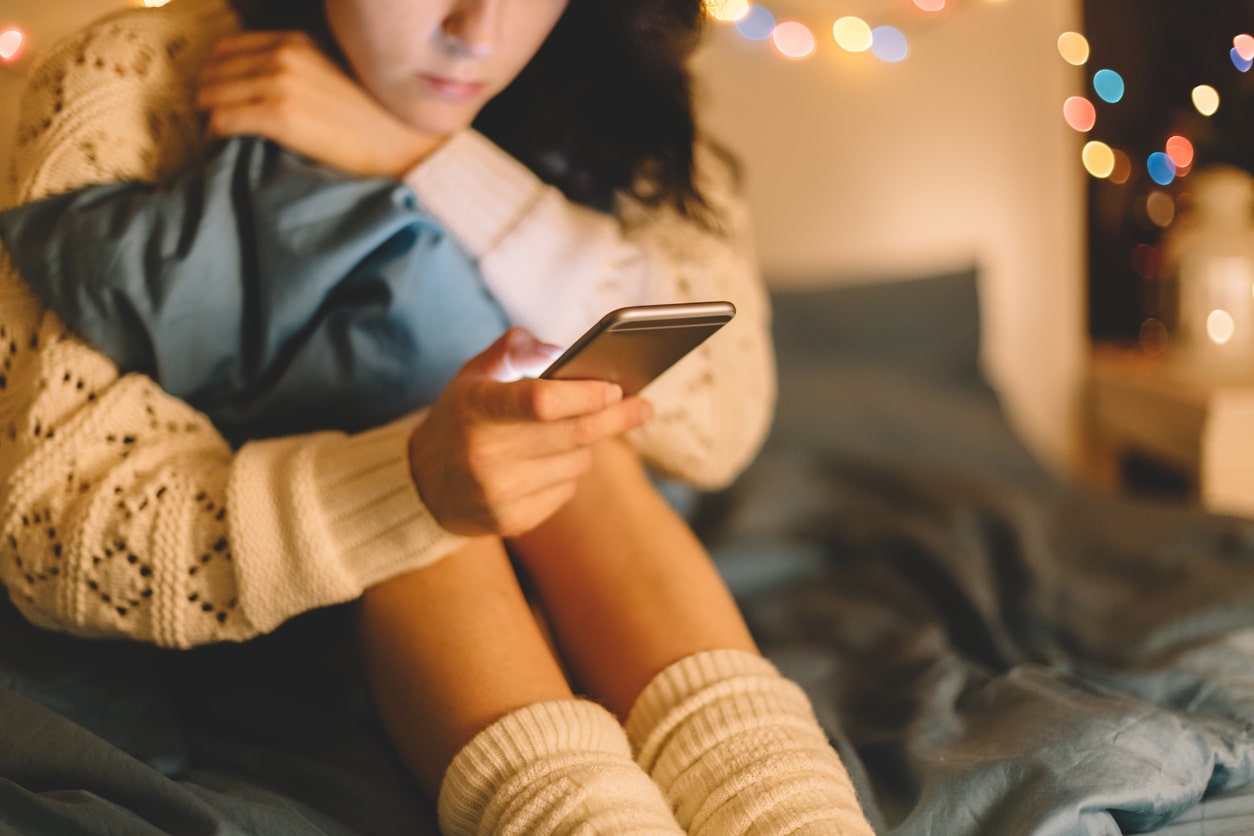 Teenage girl sits on her phone in her bedroom.