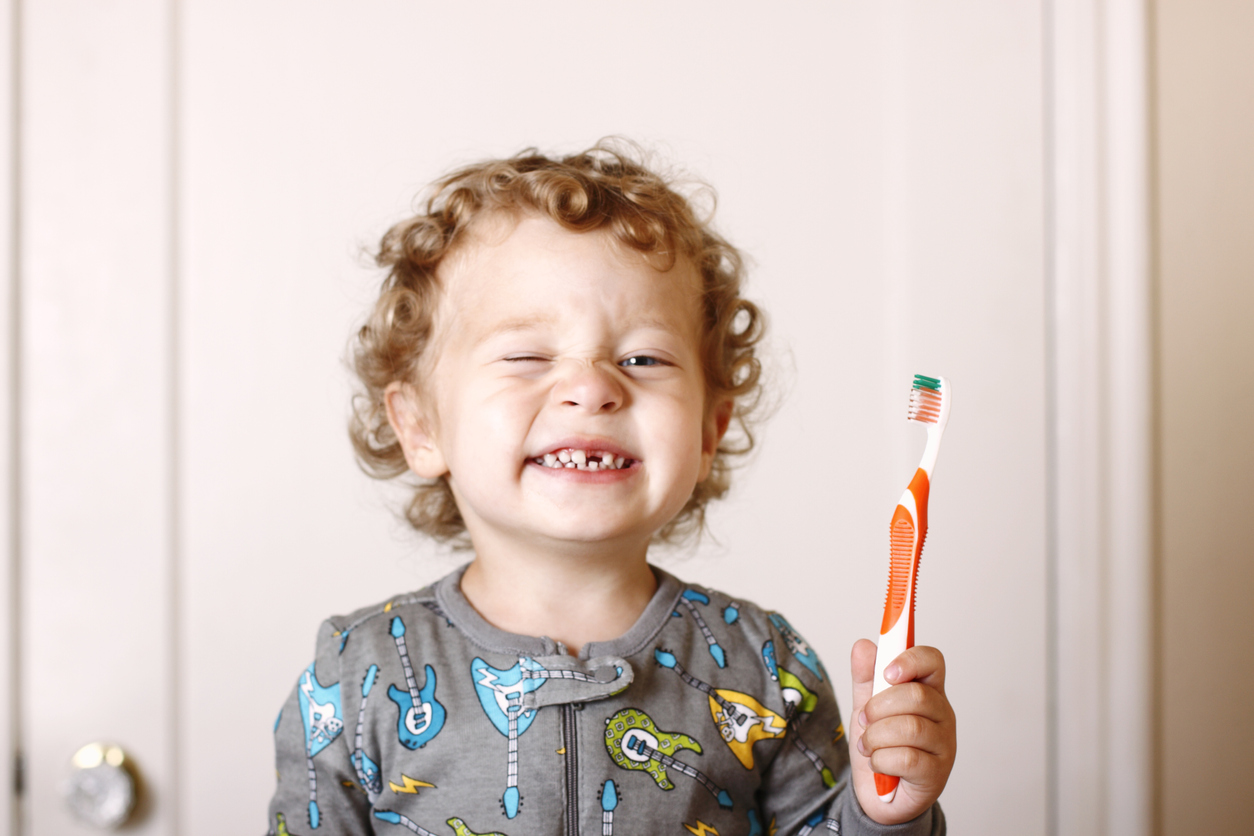 A three year old toddler in his pajamas brushing his teeth. Front tooth missing.