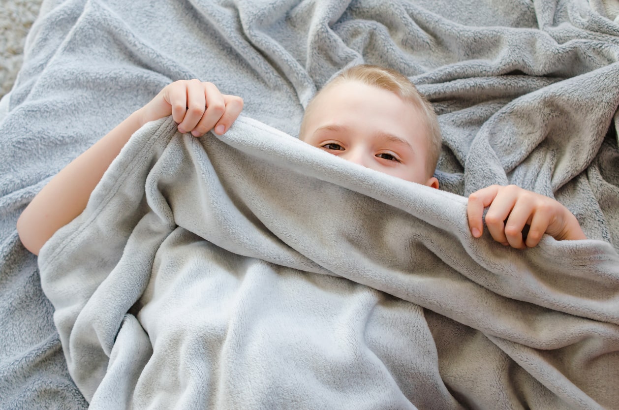 Young boy with ADHD sits under weighted blanket gift