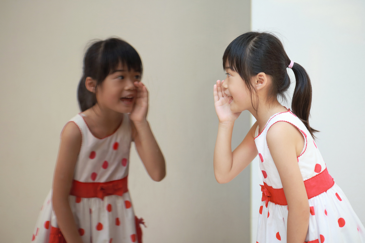little girl whispers to herself through a mirror