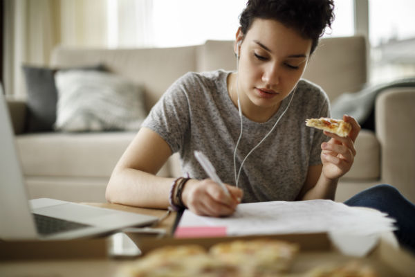 distracted teen doing homework and eating pizza
