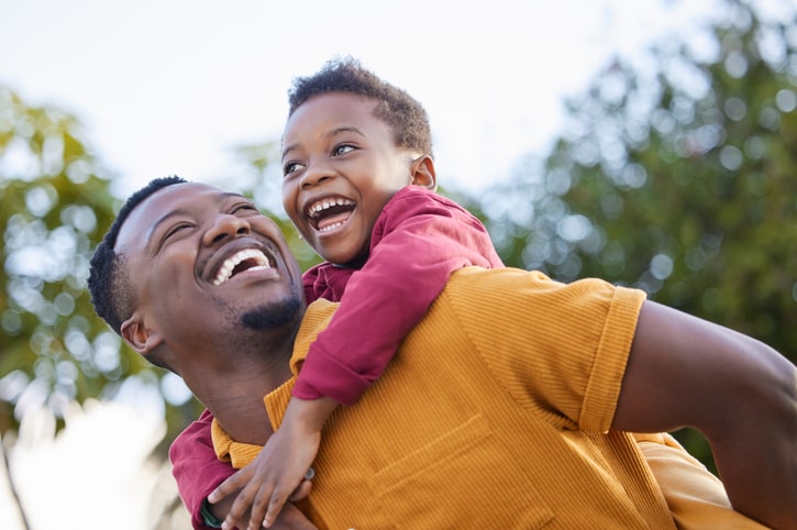 hot of an adorable little boy enjoying a piggyback ride with his father in a garden