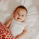 smiling baby laying on bed surrounded by strawberry-themed blanket and pillow