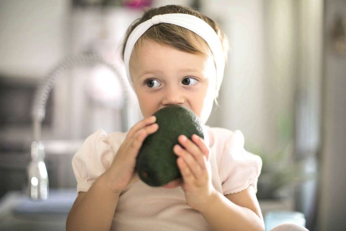 little girl biting avocado as part of keto diet