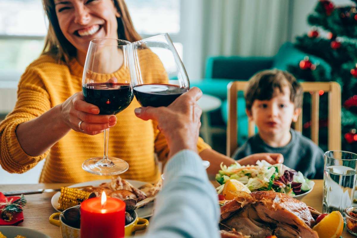 Two adults holding wine over dinner table, having Friendsgiving with their kid