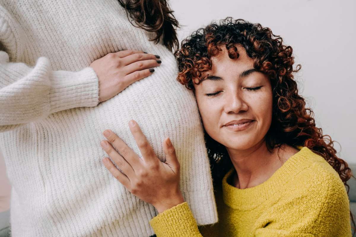 LGBT lesbian pregnant woman having tender moment listening her wife baby belly