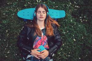 Relaxed teen listening to music on the ground with head lying on top of mini cruiser skateboard