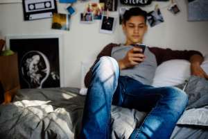 Boy with chronic illness in college dorm scrolling on his phone 