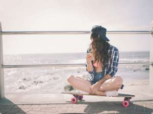 VSCO girl teen on skateboard at beach