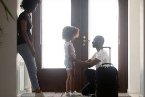 African dad talking to upset mixed race kid daughter leaving family with suitcase in hallway