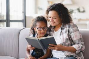 African-american mother mom reading fairy tales book novel with daughter girl, learning together, helping assisting with homework for school. Female tutor teaches schoolgirl at home. Homeschooling
