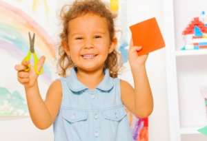 Smilling little girl holding scissors and a paper square