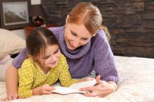Summer Reading for Kids, Girl reading book with mother on a bed