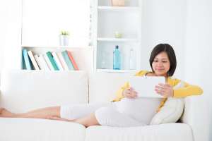 Pregnant woman reading tablet on couch