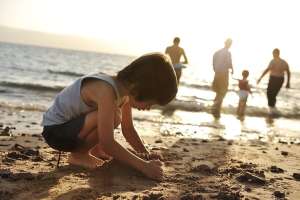 Child playing in the sand with family in the background