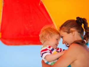 Mom and baby sitting under umbrella at the beach