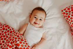 smiling baby laying on bed surrounded by strawberry-themed blanket and pillow