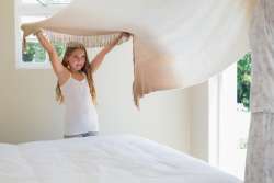 Young girl making her bed with her mom