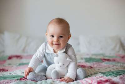Baby sitting on a bed holding a stuffed animal 