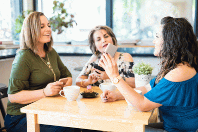 3 women at a table chatting about funny gifs on a phone