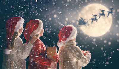3 kids looking at Santa and his reindeer under moonlight sky.