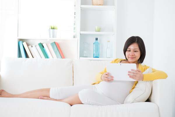Pregnant woman reading tablet on couch