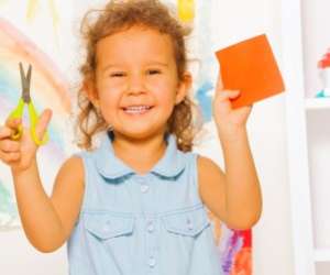 Smilling little girl holding scissors and a paper square