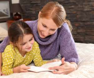 Summer Reading for Kids, Girl reading book with mother on a bed